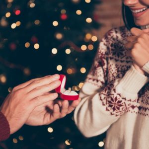 man proposing to woman in front of christmas tree